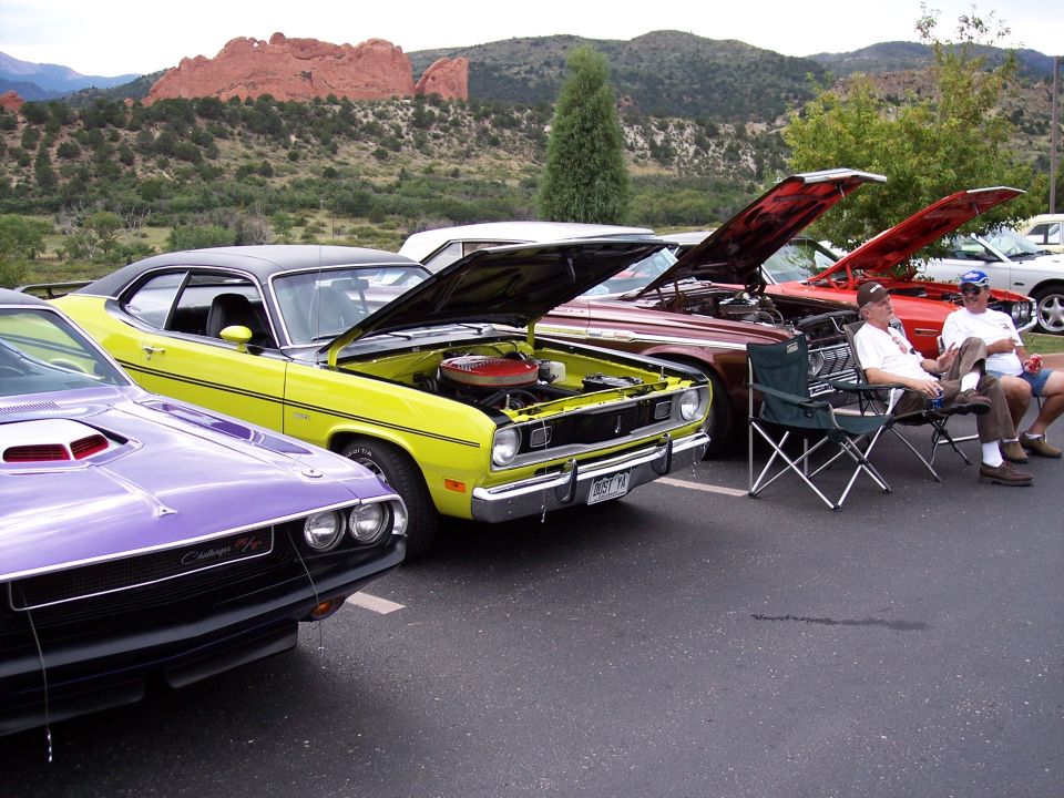 Yellow 1970s muscle car with hood open, parked next to a purple Challenger