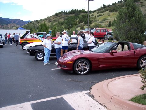 1972 Ford Ranchero - Several cars are on display with people mingling in a parking lot with a hilly background.