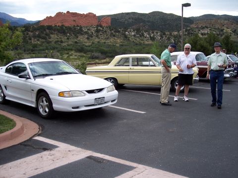 1972 Ford Ranchero - A white Ford Mustang is parked in front of a yellow Ford Falcon at a car show with people milling around.