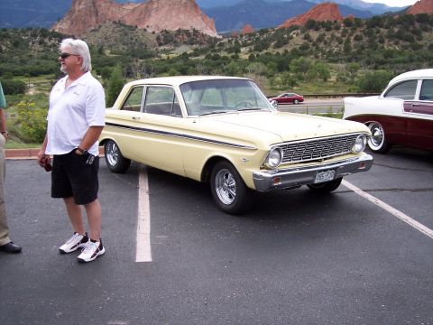 1972 Ford Ranchero - A yellow 1964 Ford Falcon sedan is parked at a scenic location, with a man standing nearby and another classic car visible.