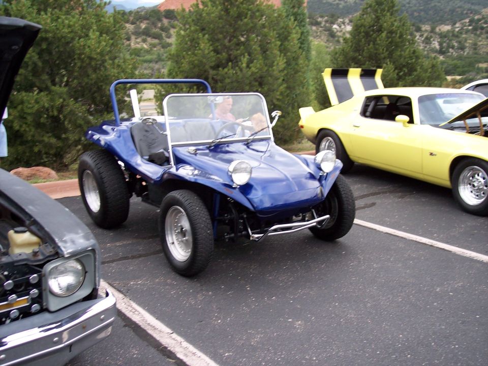 Blue dune buggy with chrome bumper and roll bar, parked next to a yellow car