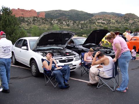 1972 Ford Ranchero - People gather around vehicles with hoods open at an outdoor event, with mountains in the background.