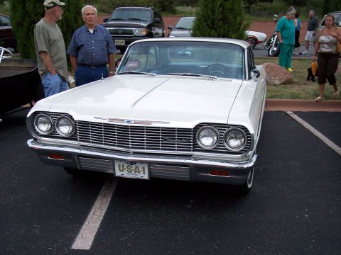1972 Ford Ranchero - A white Chevrolet sedan is parked at a car show with people around.