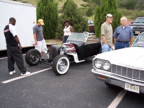 1972 Ford Ranchero - A custom hot rod with a prominent V8 engine is displayed next to a white car at an outdoor event.
