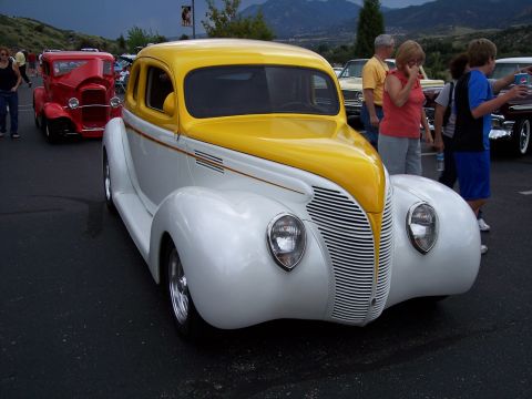 1972 Ford Ranchero - A classic yellow and white coupe is parked at an outdoor car show with people milling around.