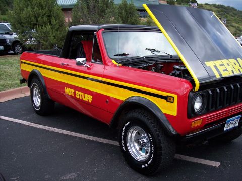 1972 Ford Ranchero - A red and yellow pickup truck with its hood open is parked on asphalt.