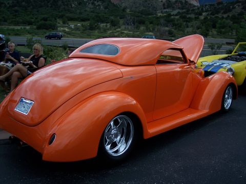 1972 Ford Ranchero - An orange hot rod coupe with its hood open is parked next to a yellow vehicle at a car show.