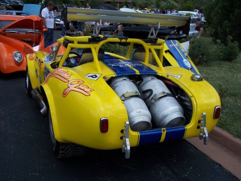 1972 Ford Ranchero - A custom yellow race car with a prominent rear spoiler and exposed propane tanks is parked next to an orange car.