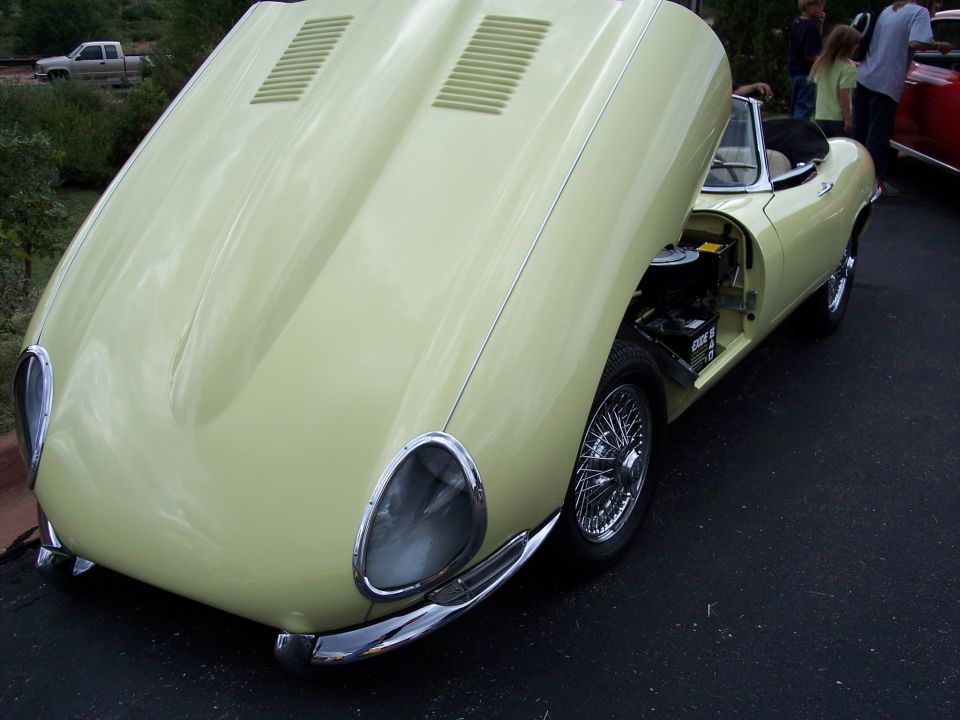 Yellow convertible sports car, hood open, wire wheels, chrome bumper, visible battery