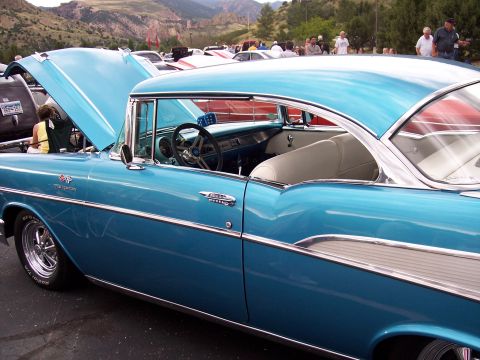 1972 Ford Ranchero - A classic blue 1957 Chevrolet Bel Air is displayed with its hood up at a car show, with other vehicles and people visible.