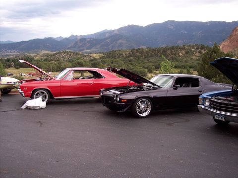 1972 Ford Ranchero - A black muscle car with its hood open is parked alongside other vehicles with a scenic mountain backdrop.