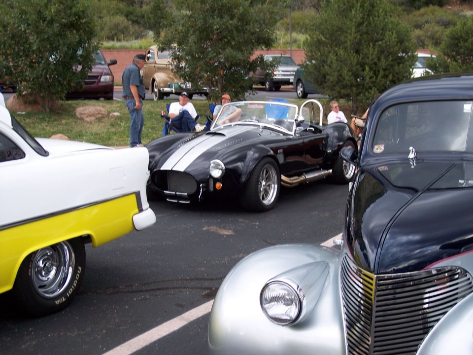 Black convertible sports car with dual white racing stripes, chrome exhaust pipes, and silver wheels