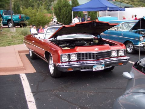 1972 Ford Ranchero - A red convertible with its hood open is parked at an outdoor event, revealing its engine and chrome grille. Another blue classic car is vis…