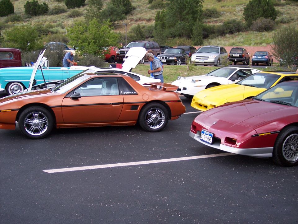 Orange Pontiac Fiero with a spoiler and chrome wheels, parked on asphalt