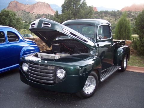 1972 Ford Ranchero - A classic green Ford pickup truck is displayed with its hood open, parked outdoors with mountains in the distance.