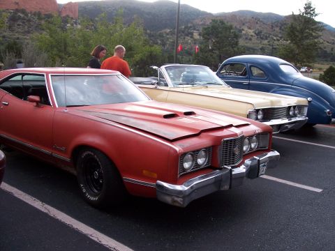 1972 Ford Ranchero - A red 1972 Ford Ranchero is parked in a lot with other classic cars, with mountains in the background.