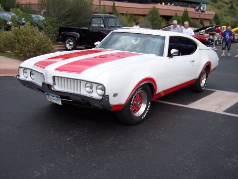 1972 Ford Ranchero - A white 1970 Oldsmobile 442 with red racing stripes and trim is parked at an outdoor event.