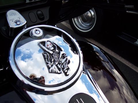 1972 Ford Ranchero - A chrome gas tank cap on a motorcycle features a grim reaper emblem, reflecting the sky and a photographer.