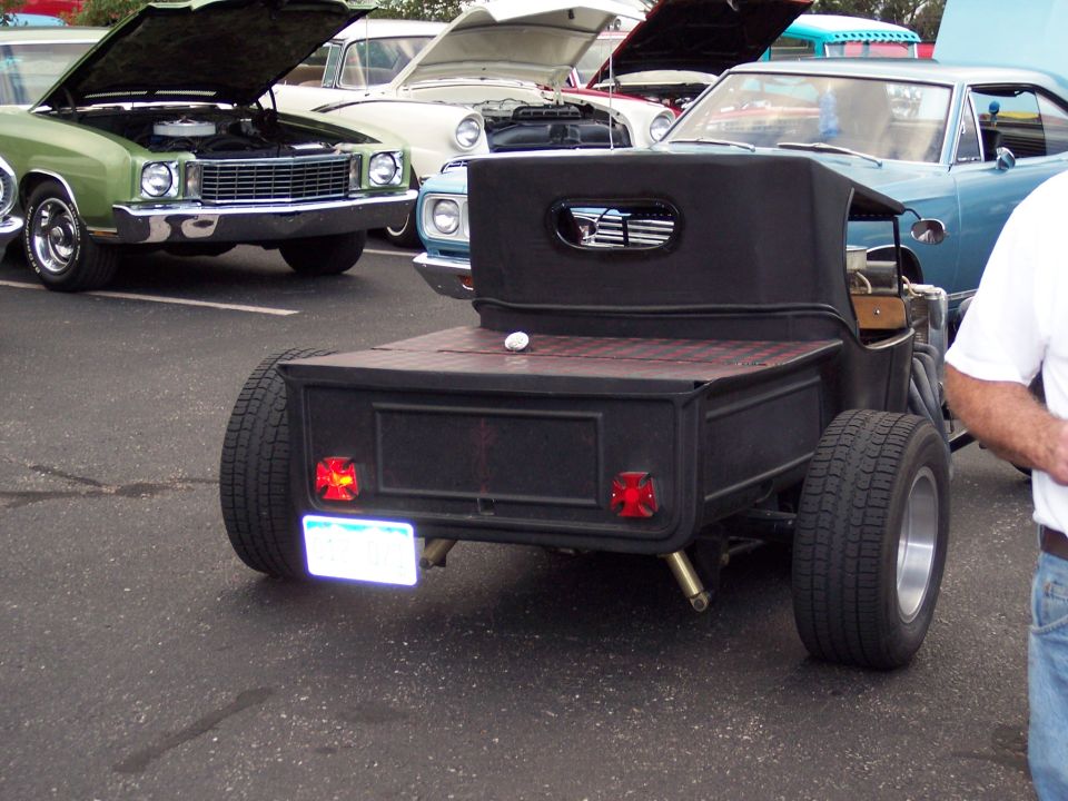 Black hot rod pickup truck rear view, custom bed, red cross-shaped taillights, wide tires