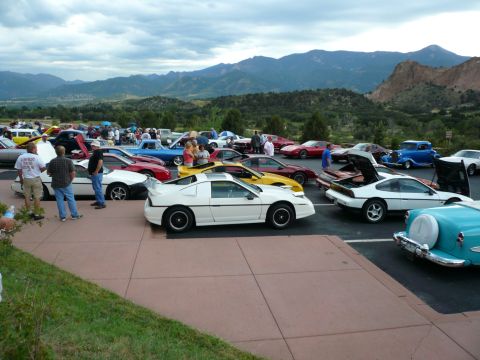 1975 Ford Ranchero - A gathering of various cars is displayed with a scenic mountain backdrop under a cloudy sky.