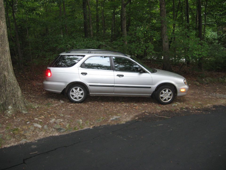 Silver compact station wagon parked on dirt at the edge of a forest