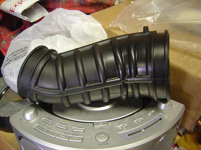 Black rubber air intake hose on a silver CD player, with plastic bags and cardboard boxes in the background