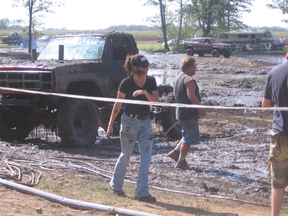 Muddy GMC pickup truck with people around it at a mud bog event