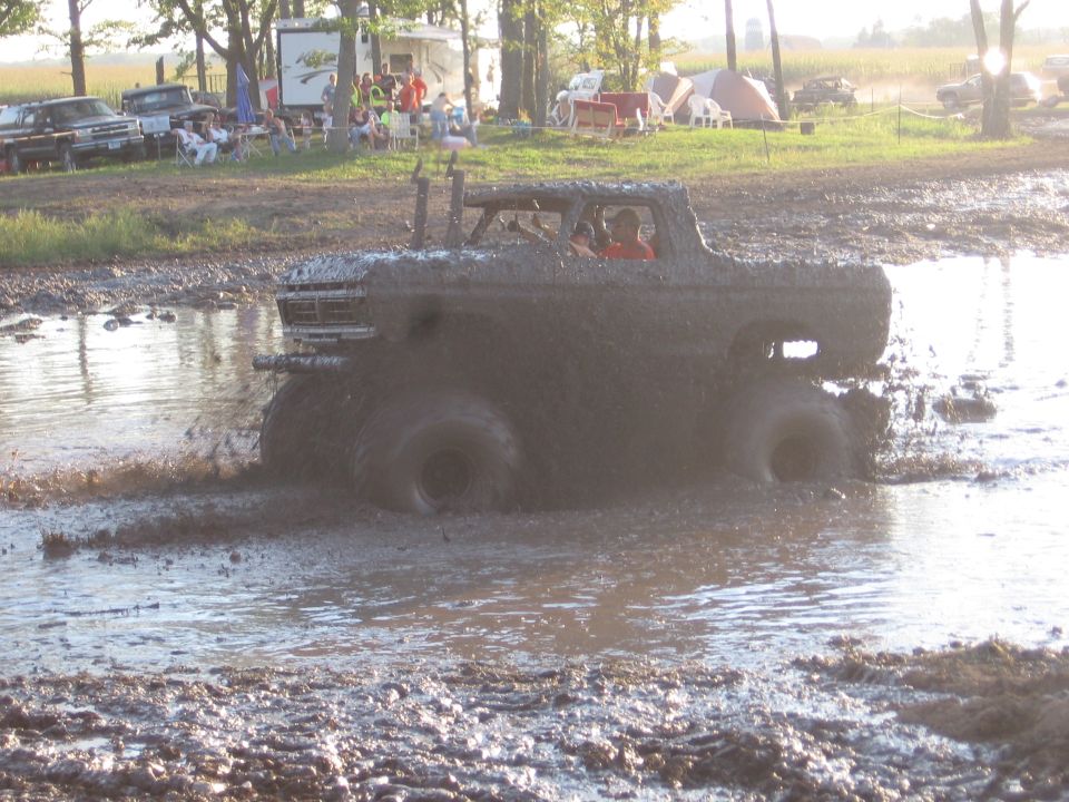 Mud bogging truck with large tires splashing through a muddy pool