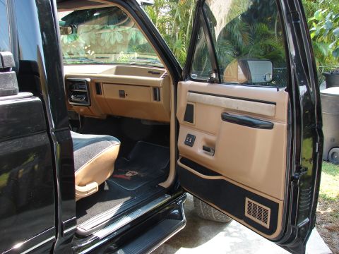 1987 Ford F-150 - The tan interior of a black pickup truck features a two-tone seat and a clean dashboard.