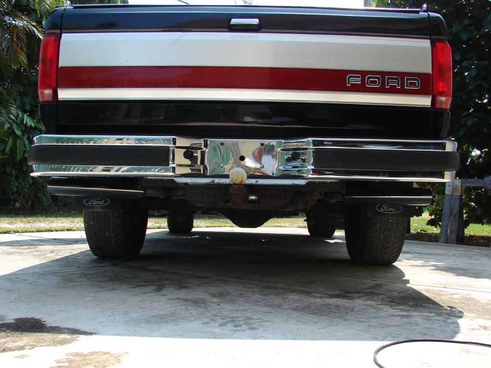 Rear view of a two-tone Ford pickup tailgate with chrome step bumper and ball hitch