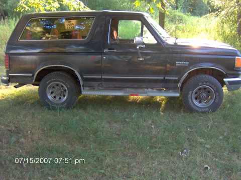 1987 Ford Bronco - Side profile of a 1987 Ford Bronco parked outdoors in grassy area.