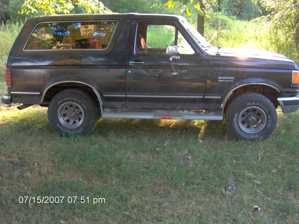 Black Ford Bronco passenger side profile parked on grass with all-terrain tires