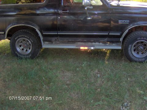 1987 Ford Bronco - The side of a black Ford Bronco is shown, its running boards and tires.