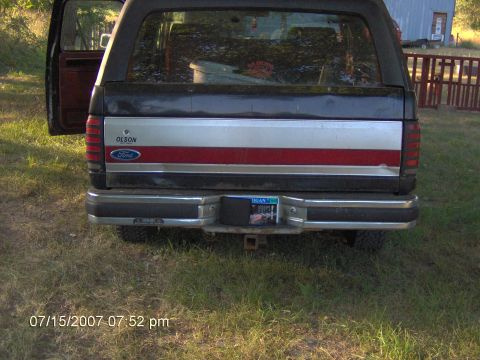 1987 Ford Bronco - Rear view of a black Ford Bronco with a distinctive red and silver stripe on the tailgate.