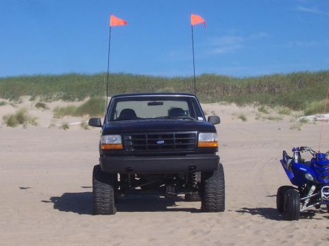 1994 Ford F-150 - Lifted 1994 Ford F-150 parked on a sandy beach with dunes and a blue ATV nearby.