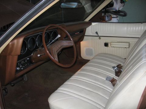 1975 Ford Ranchero - The interior of a 1975 Ford Ranchero shows a brown dashboard and a tan bench seat with seatbelts.