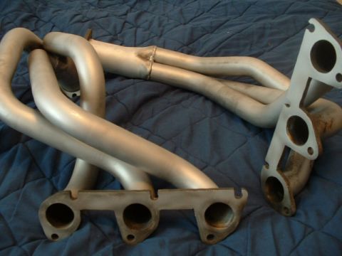1992 Ford Probe - Exhaust manifold pipes with two mounting flanges are shown on a blue quilted surface.