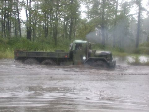 1986 Ford F-250 - Military truck navigating through a muddy, wooded area.