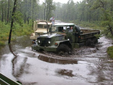 1986 Ford F-250 - Military trucks navigate a challenging off-road course through water and mud.