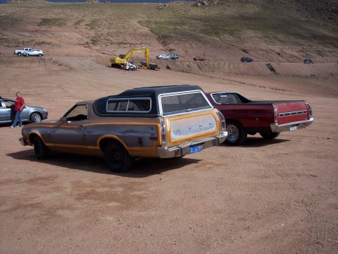 1972 Ford Ranchero - Two pickup trucks with camper shells are parked on a dirt road with an excavator in the background.