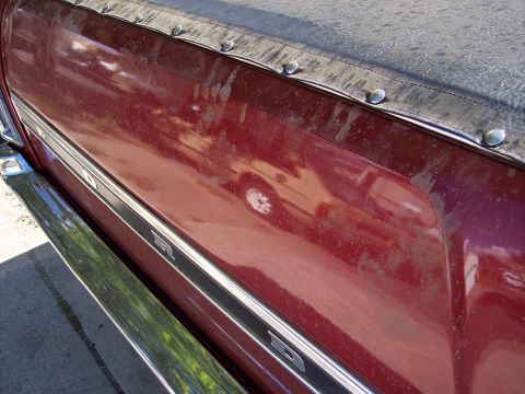 1972 Ford Ranchero - A side view of a red vehicle with a chrome bumper and a black tonneau cover, showing dust and reflections.