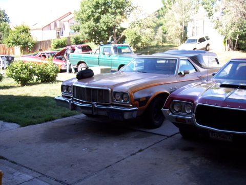1972 Ford Ranchero - Multiple vehicles are parked in a driveway on a sunny day. The foreground shows a tan and orange 1972 Ford Ranchero.