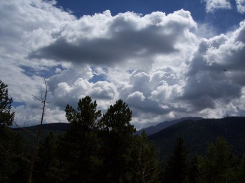 1972 Ford Ranchero - Dramatic clouds gather over a dark, forested mountain range under a bright blue sky.