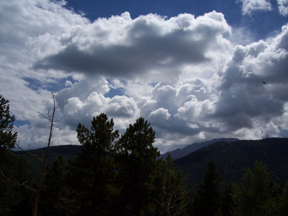 Stormy sky with dramatic clouds over dark, forested mountains