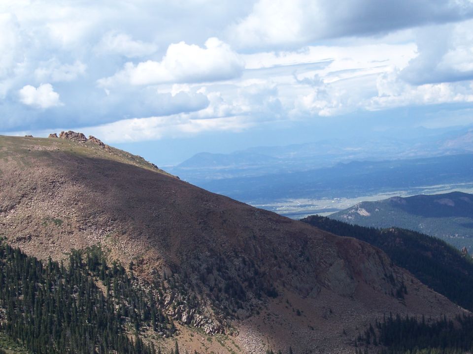 Mountain landscape with rocky slopes and distant valley under cloudy sky
