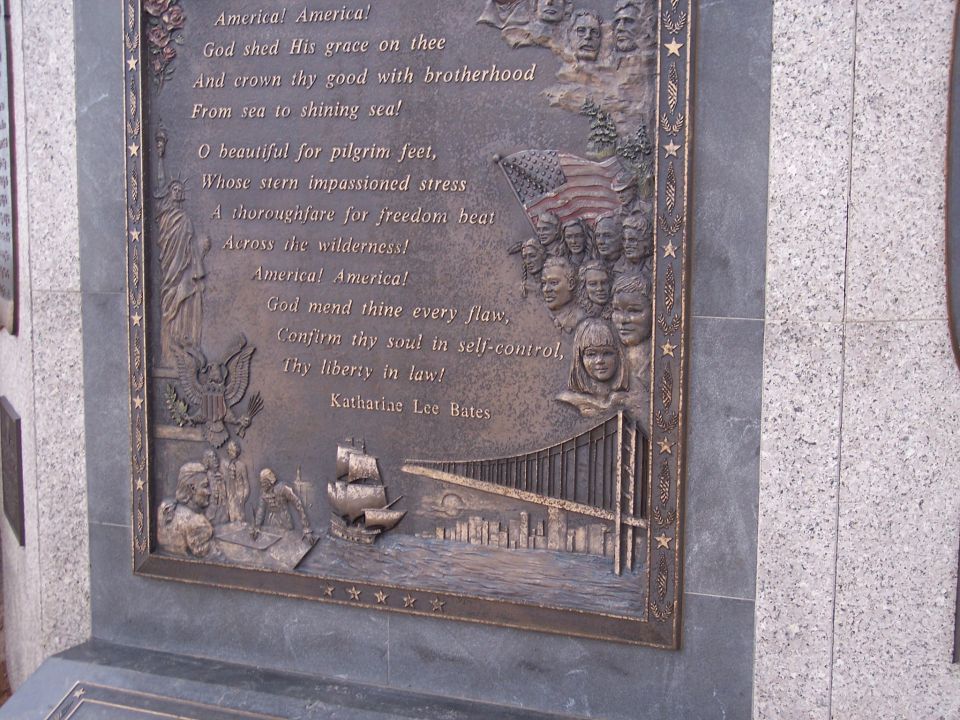 Bronze relief on a monument shows text of America the Beautiful poem, Statue of Liberty, ship, bridge, and city skyline