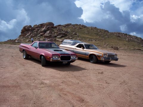 1972 Ford Ranchero - Two Ford Rancheros are parked on a dirt road at a scenic overlook with a rocky hillside and cloudy sky.