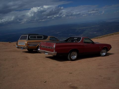 1972 Ford Ranchero - Two pickup trucks, including a red 1972 Ford Ranchero, are parked on a dirt road with a scenic mountain view.