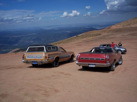 1972 Ford Ranchero - Two Ford Rancheros, one red and one tan with a camper shell, are parked on a dirt road with a scenic mountain view.