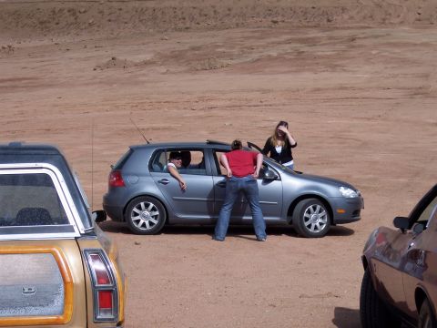 1972 Ford Ranchero - People interact around a gray Volkswagen Golf in a dirt lot with other vehicles present.